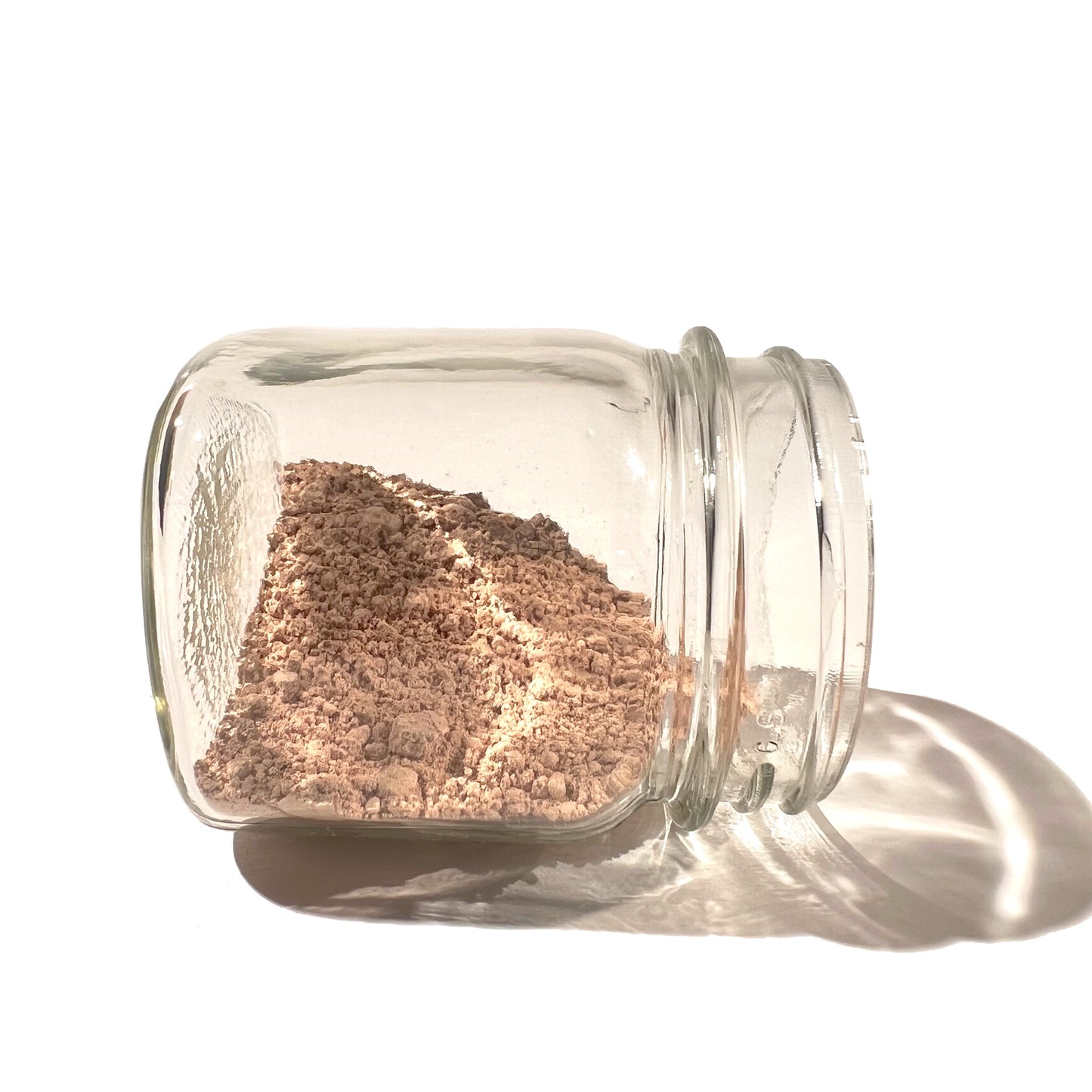 Clear glass jar on its side, half full of slippery elm bark beige powder