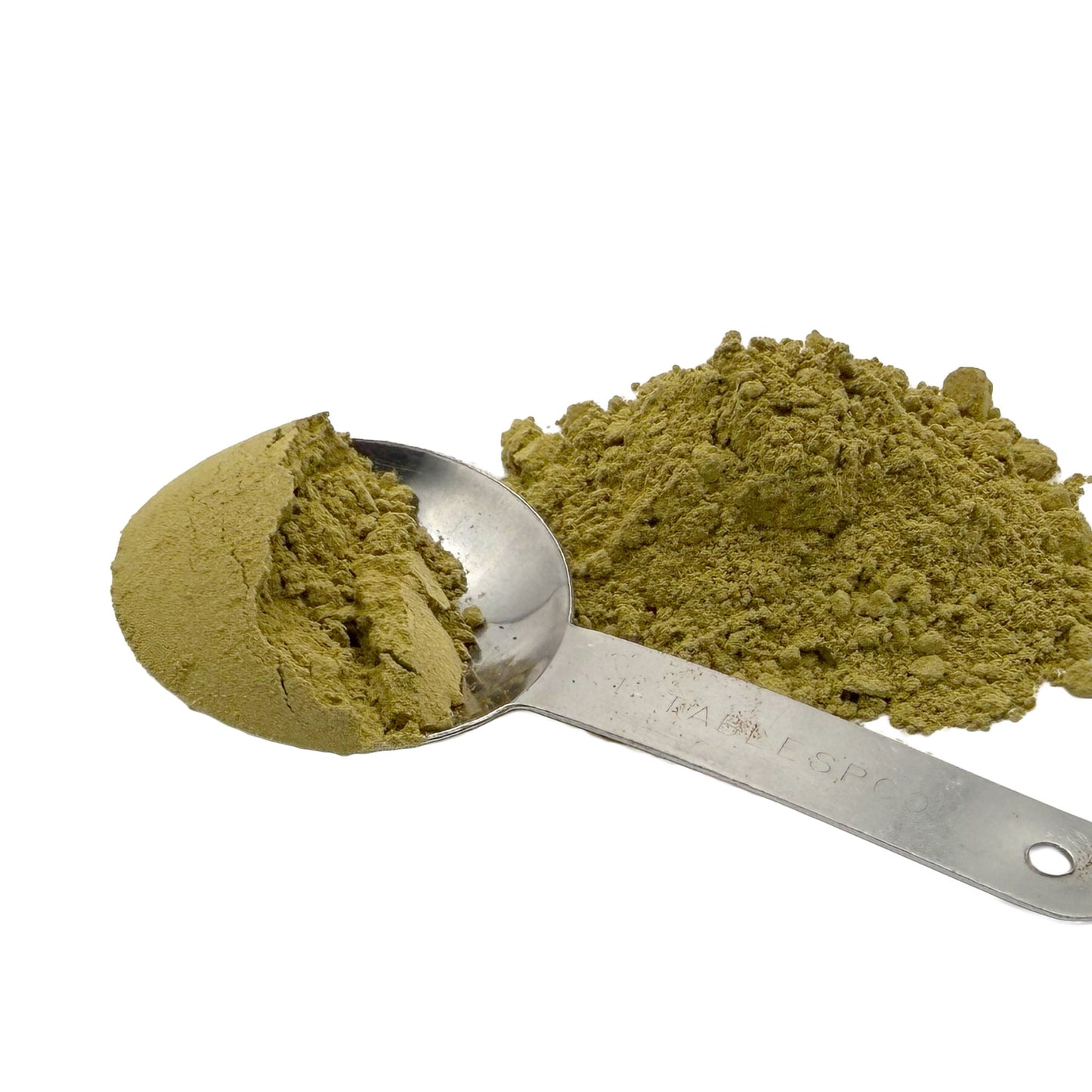 A metal measuring spoon filled with a light olive-green senna leaf powder next to a small pile of the same powder on a white background.