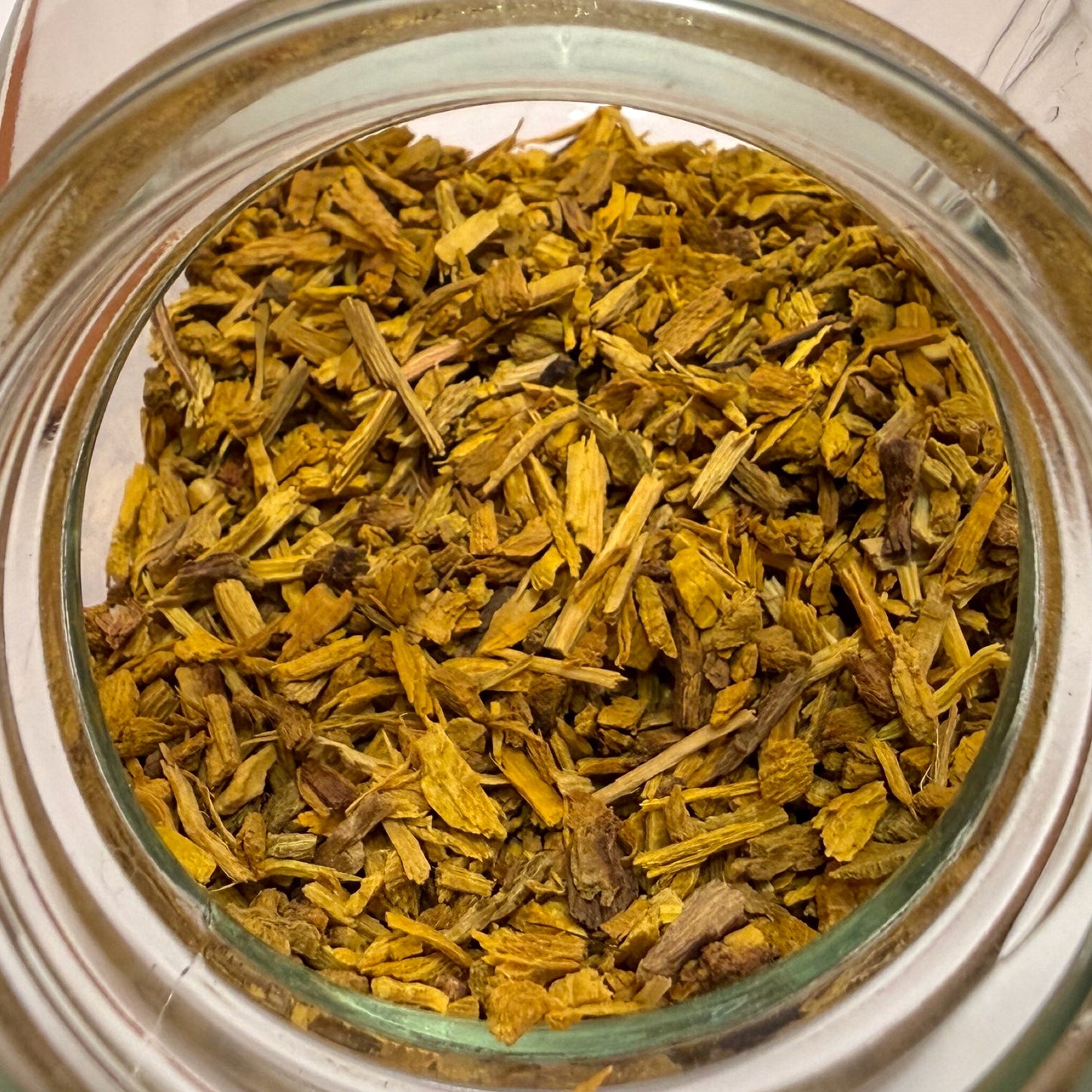 Close-up of a glass jar filled with dried yellow bark pieces on a white background