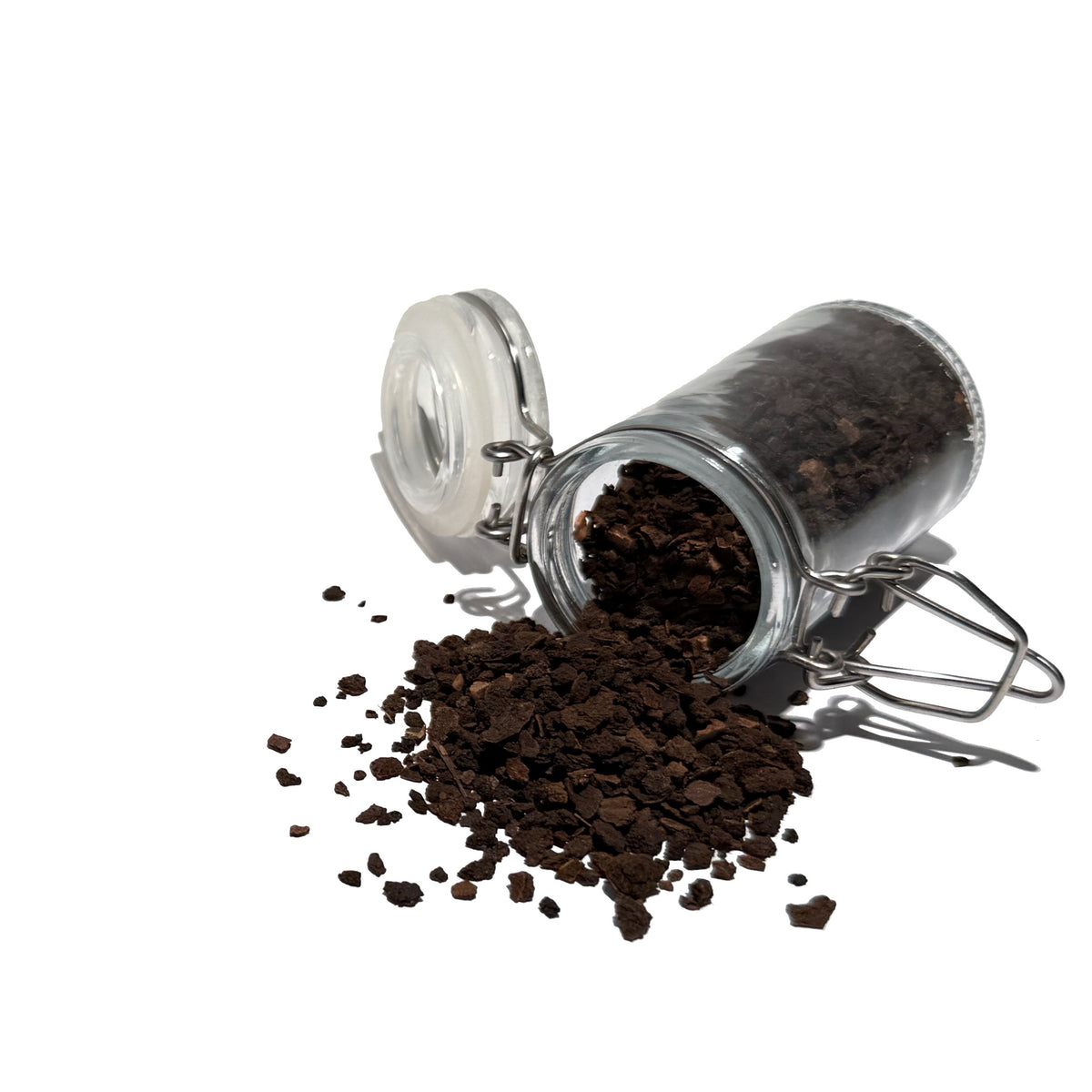 Small black walnut hull pieces spilling from an overturned glass spice jar
