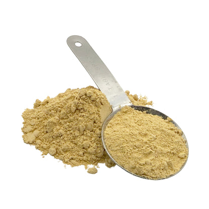 A metal measuring scoop filled with and beside a small pile of light tan powder on a plain white background.