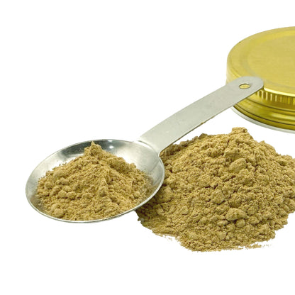 A pile and spoonful of light brown powder next to a gold-colored metal container lid on a white background.