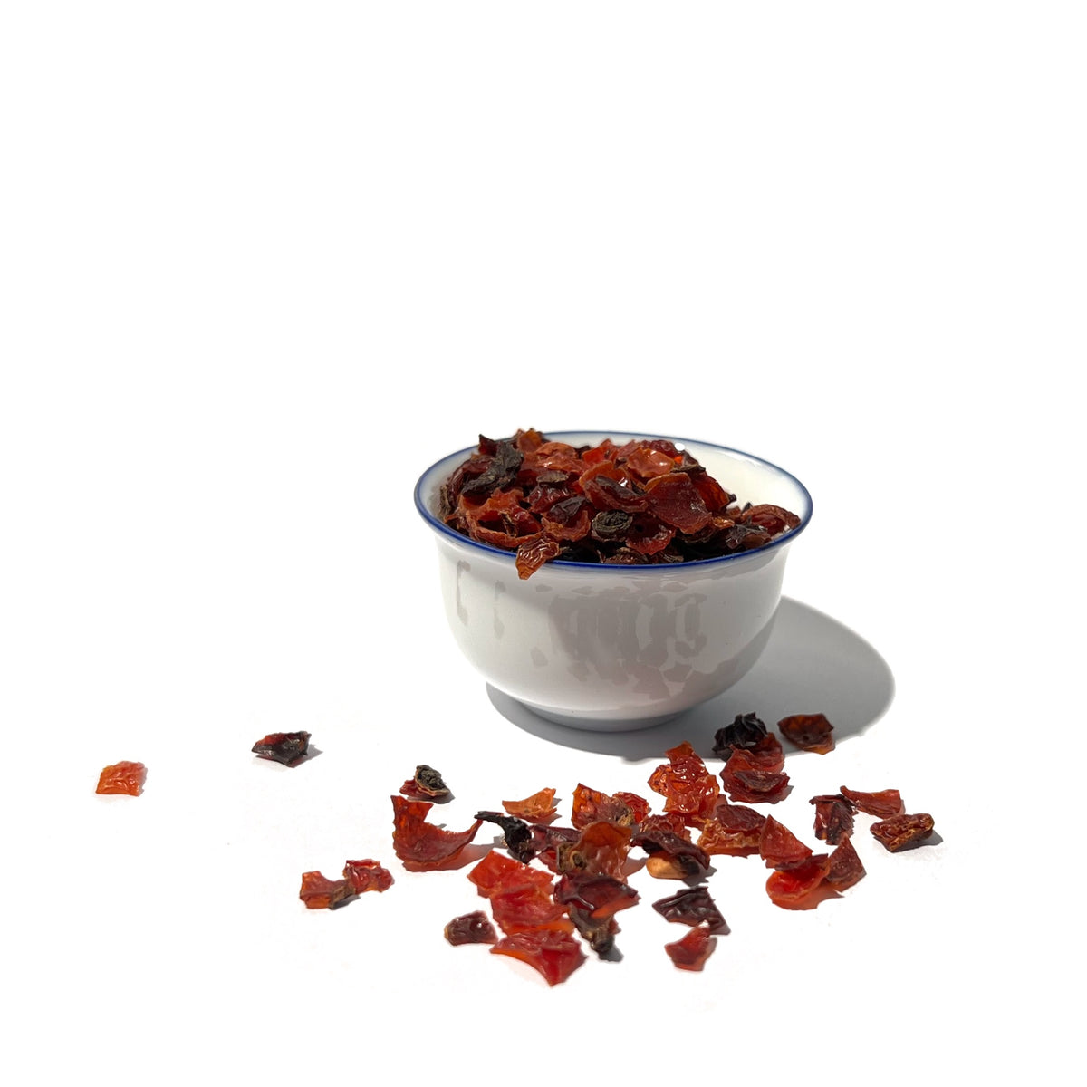 Small bowl of dried rose hip cuts with more scattered in the foreground
