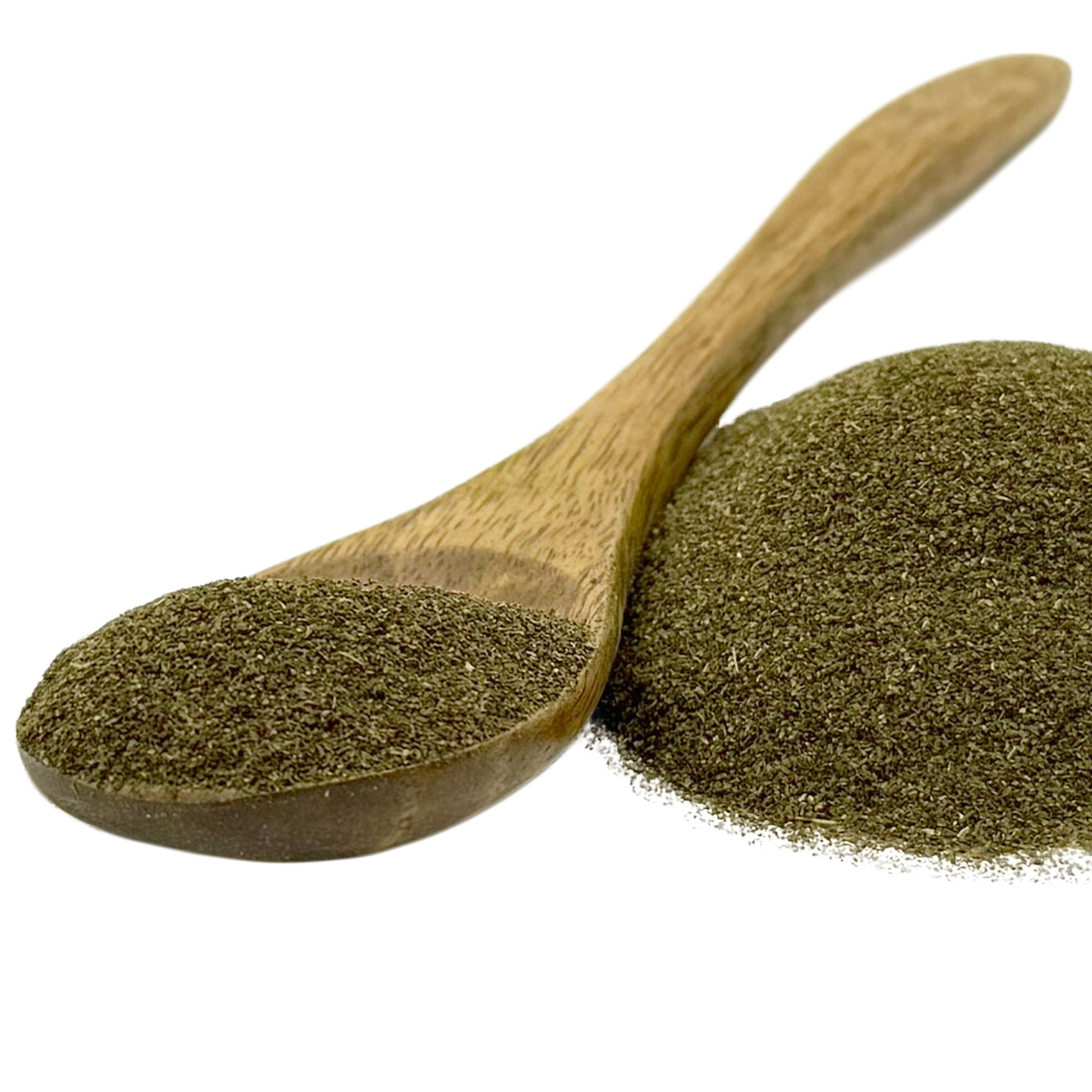 A wooden spoon filled with dark green herbal powder, with a small pile of the same powder beside it, on a plain white background.