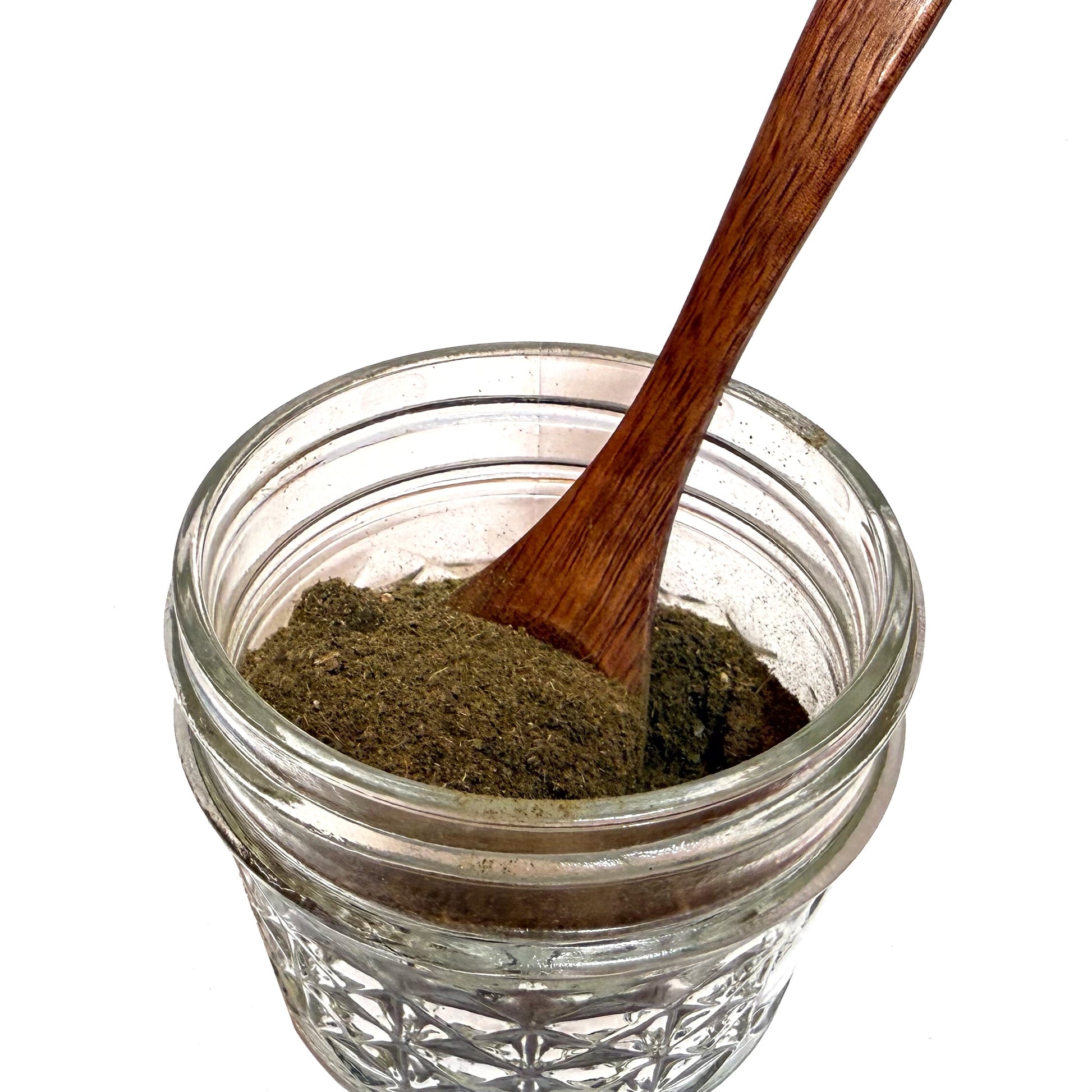 Textured glass jar partially filled with a brownish green witch hazel leaf powder and a wooden spoon