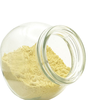 A clear glass jar tipped on its side, showing a light yellow mustard powder against a plain white background.